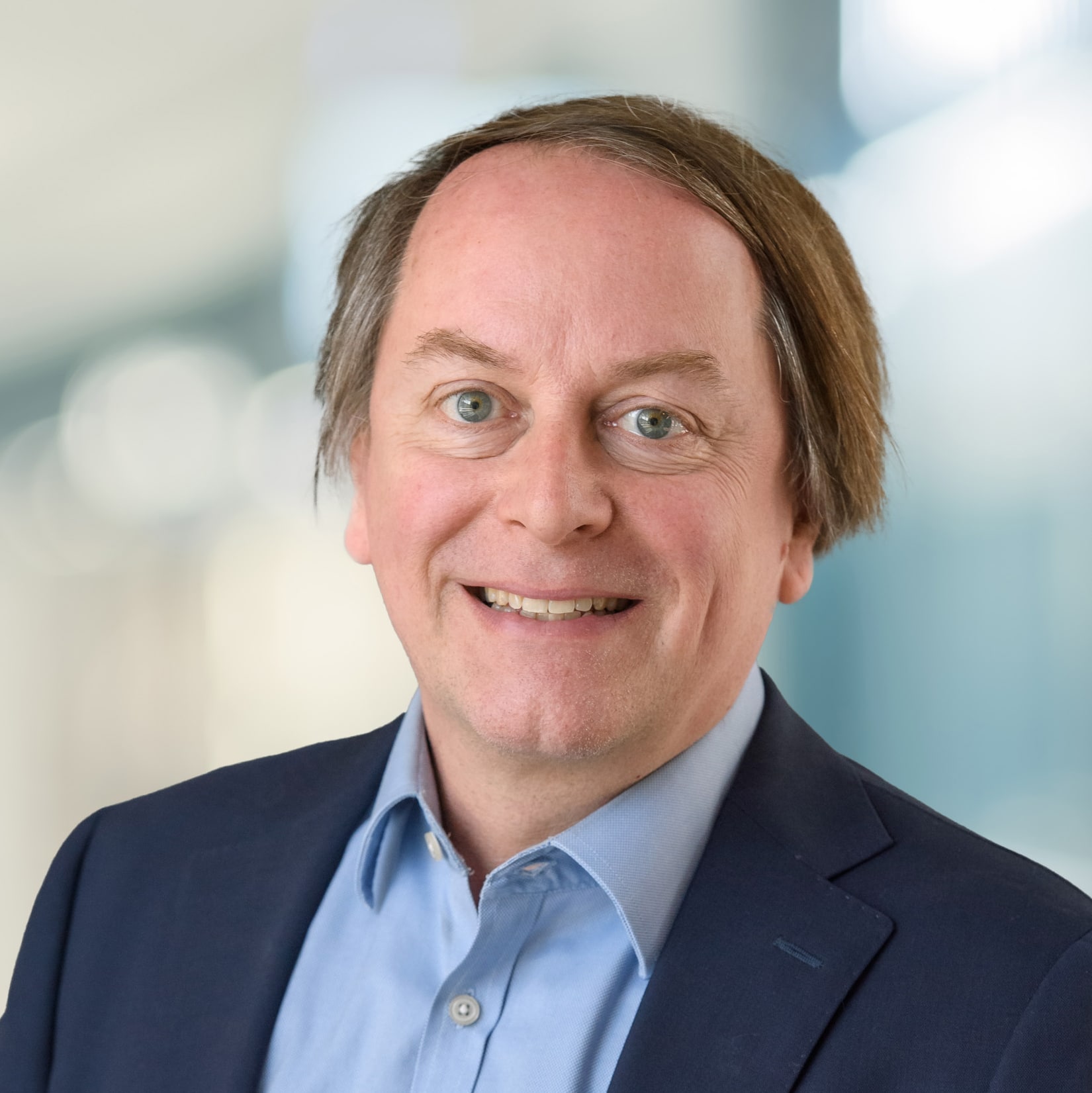 Smiling Headshot of Bruce Traversy, Investments, Dream Industrial, he wears a blue shirt with an open collar and deep blue jacket.