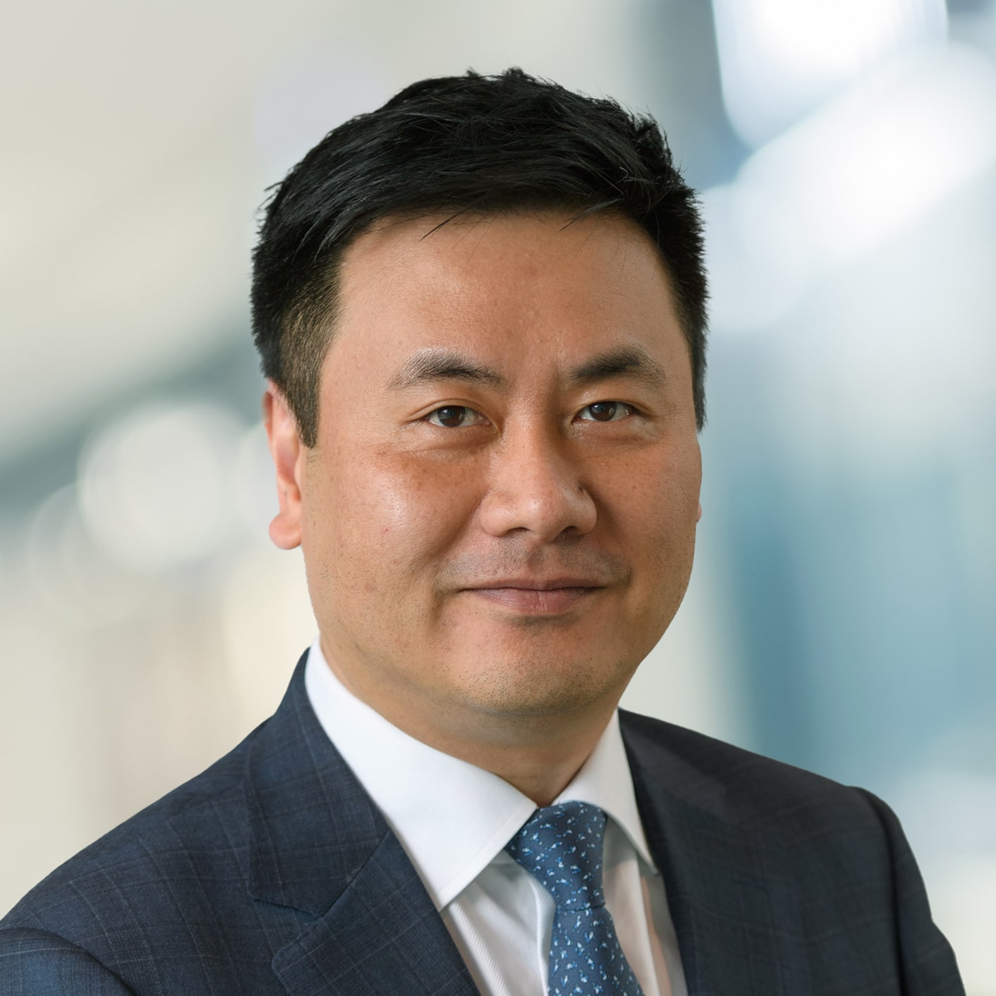 A smiling headshot of Derrick Lau, CFO, Dream Residential REIT & VP, Strategic Finance, wearing a striped blazed and spotted tie