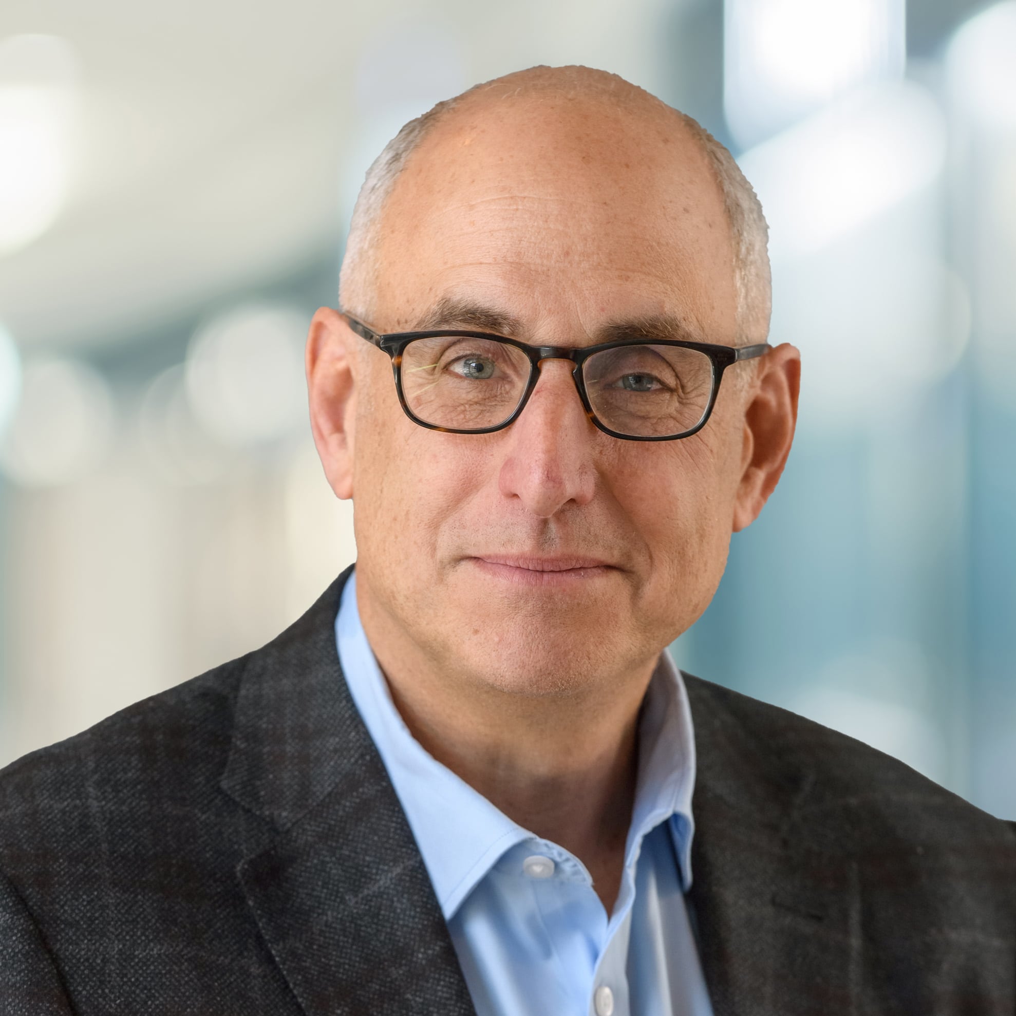 a smiling headshot of Jason Lester, Vice Chair, Development, wearing glasses, a blue button up and checkered blazer