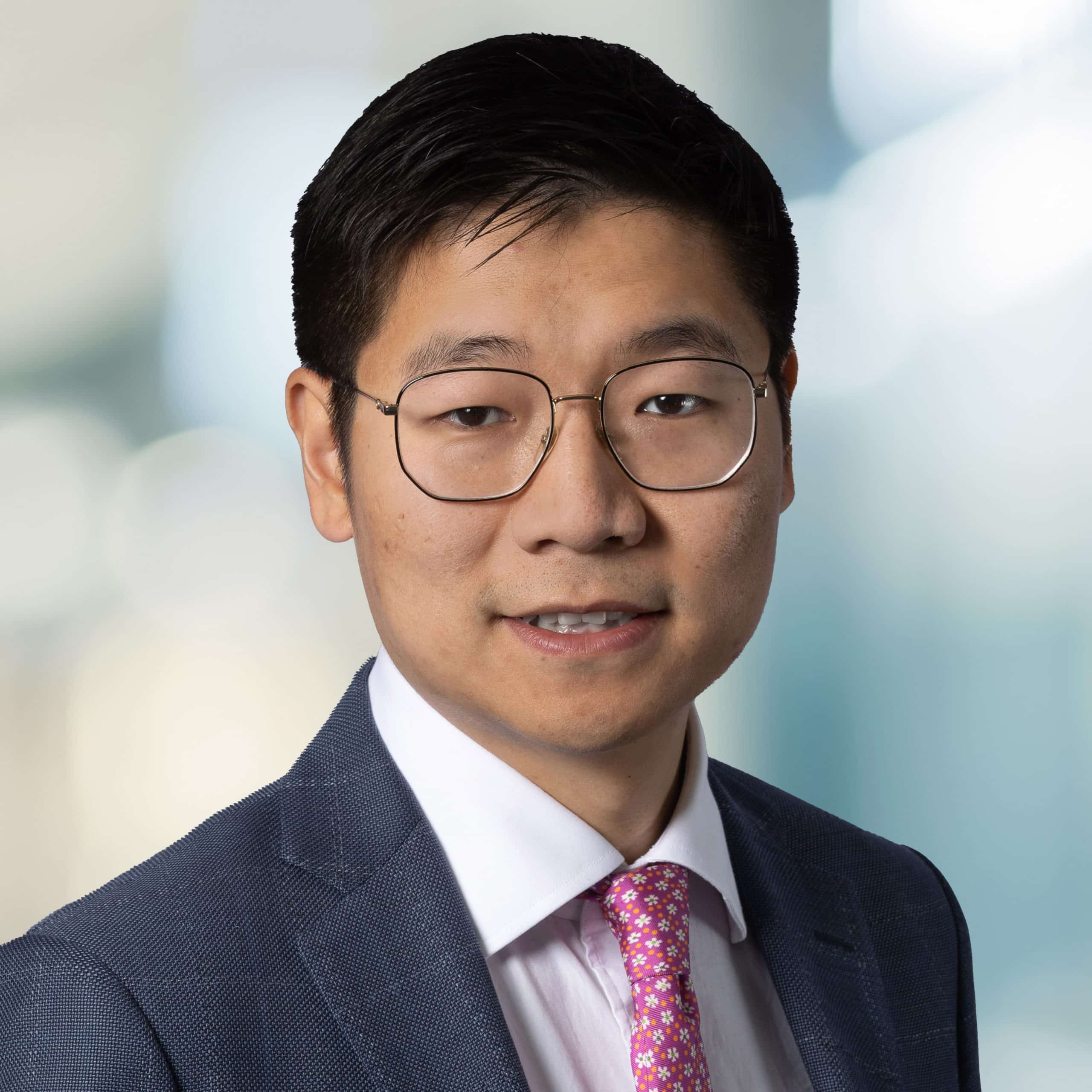headshot of Jay Jiang, CFO Dream Office Reit, wearing a blue checkered jacket with a whit button up shirt, pink tie with white flowers, and glasses