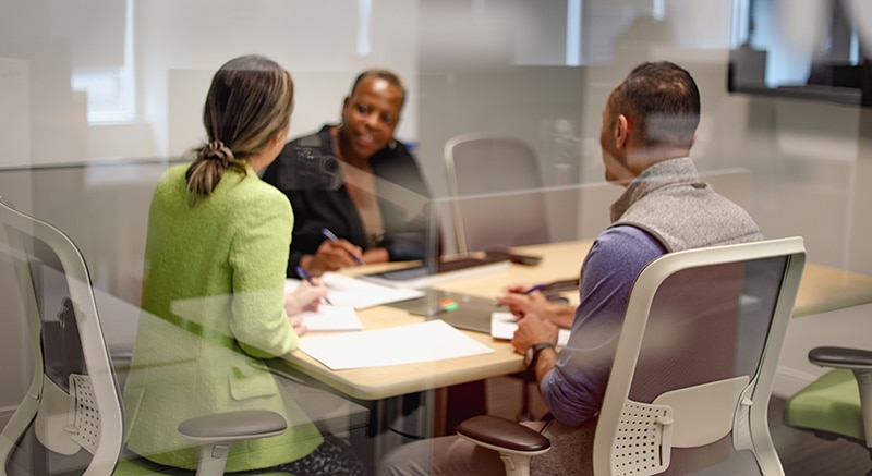 a man and two women are sitting in a meeting room, taking notes
