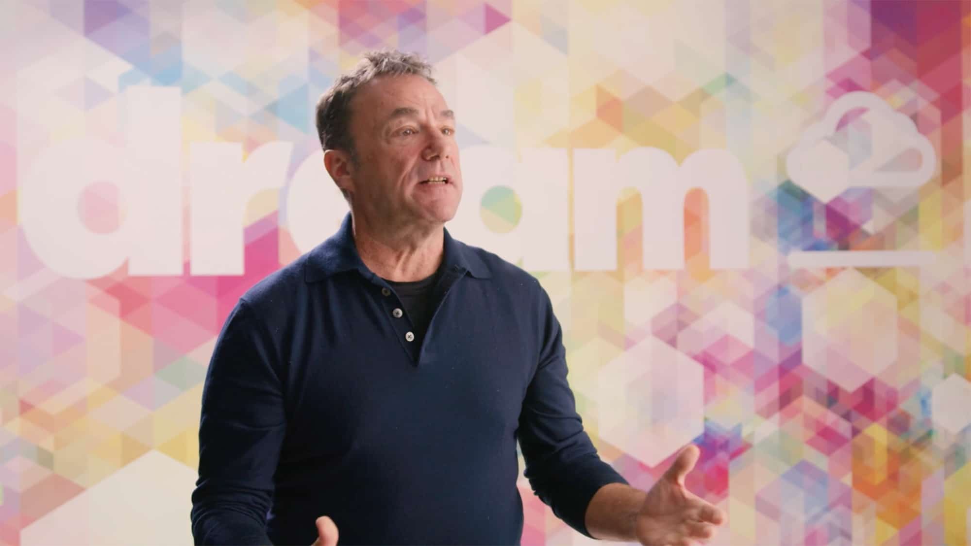 Michael Cooper, President and CRO of Dream Unlimited, gives a speech in front of a colorful mural with a kaleidoscope effect with the Dream logo, in the café at Dream Headquarters at 30 Adelaide.