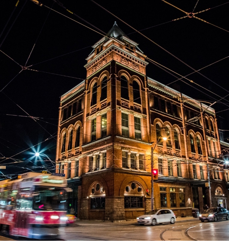 Night view of the historic Broadview Hotel with red brick architecture, arched windows, streetcar wires, passing streetcar, and a red traffic light at the Broadview intersection