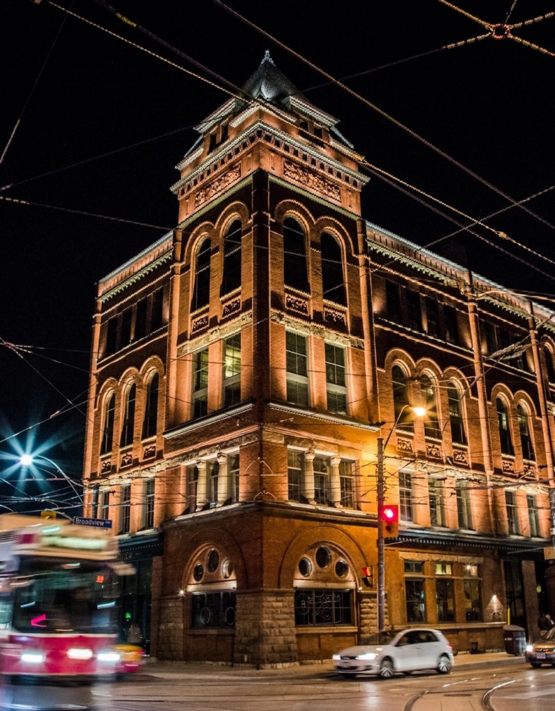 Night view of the historic Broadview Hotel with red brick architecture, arched windows, streetcar wires, passing streetcar, and a red traffic light at the Broadview intersection