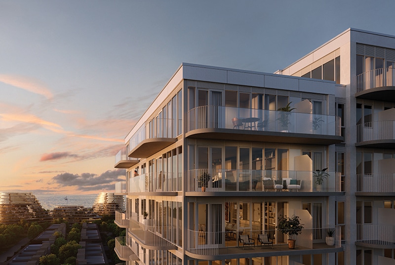 Modern multi-story residential building with glass balconies overlooking a body of water, distant buildings, and a sailboat under a partly cloudy sky at sunrise or sunset.