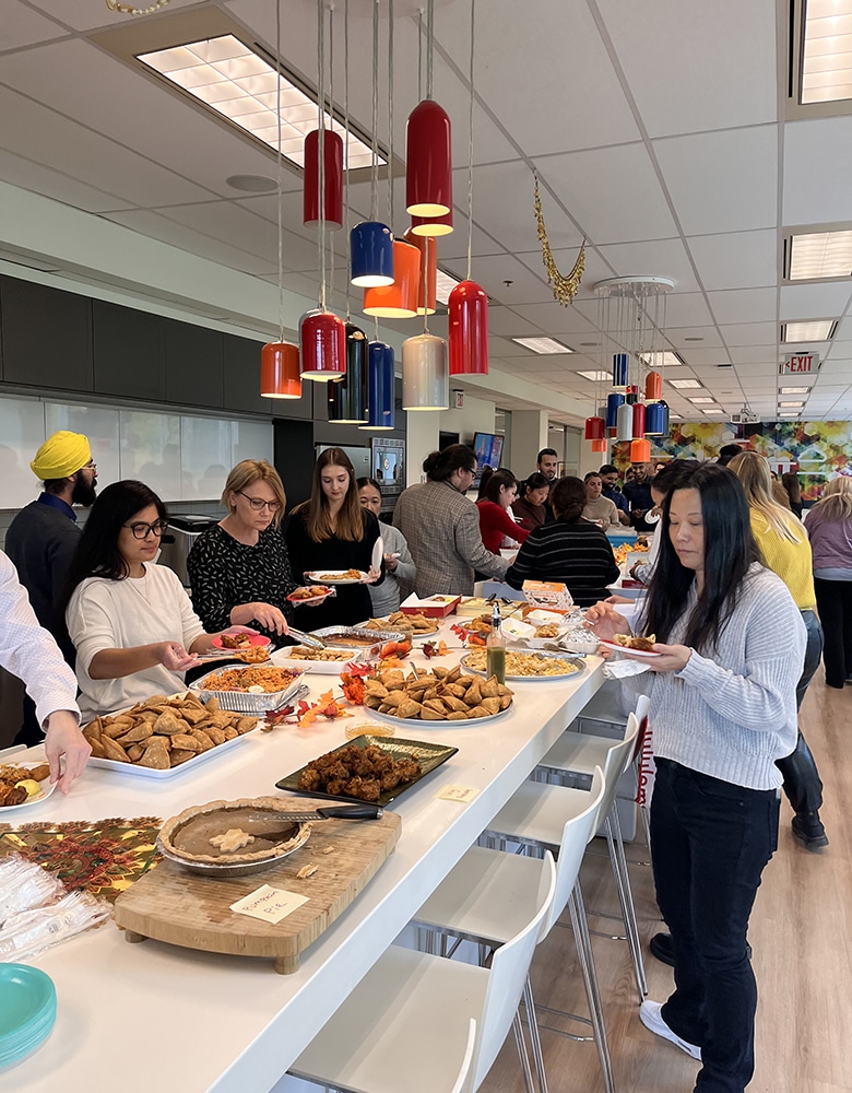 Lunar New Year celebration with people gathered around a table displaying traditional foods like egg tarts, steamed buns, and pastries; colorful lanterns hanging from the ceiling