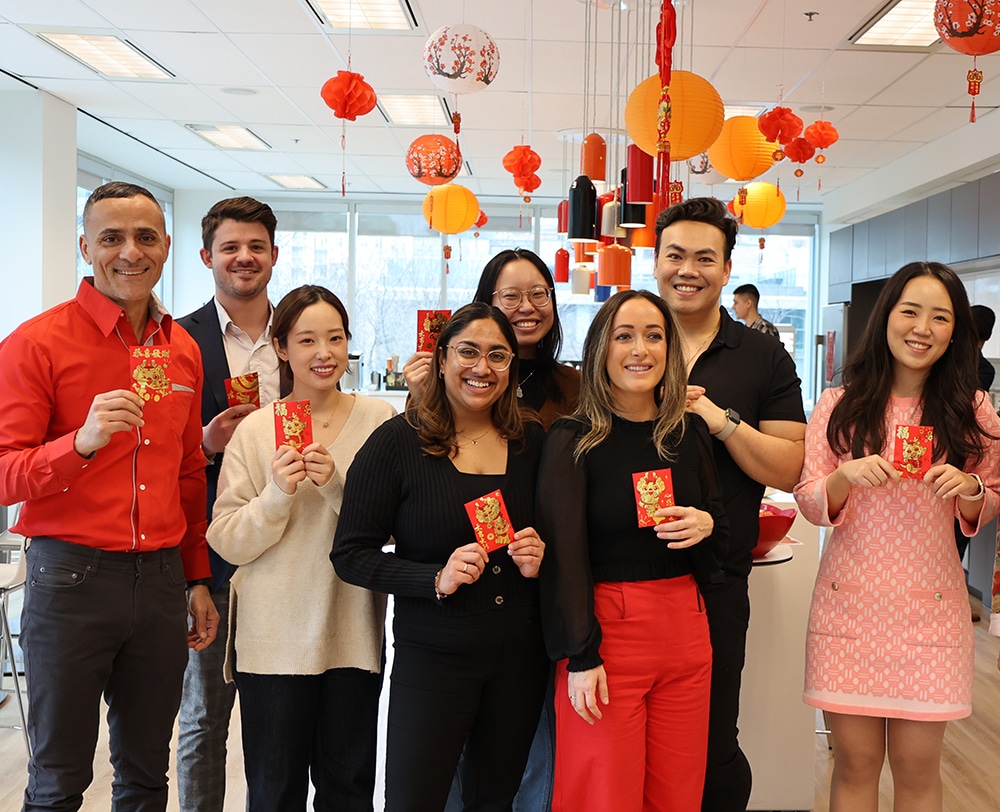 Group of people in an office celebrating Lunar New Year, holding red envelopes with festive red and orange lanterns hanging from the ceiling, members are from the Inclusion Network at Dream