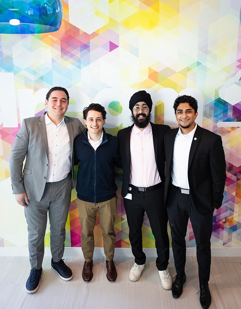 Four men in business attire standing side by side in front of a colorful geometric-patterned wall