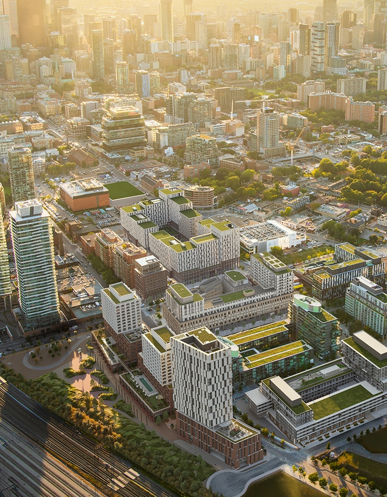 Aerial view of Canary Landing featuring modern high-rise and residential buildings with green rooftops, visible streets, trees, and a railway track, set in a densely built urban area
