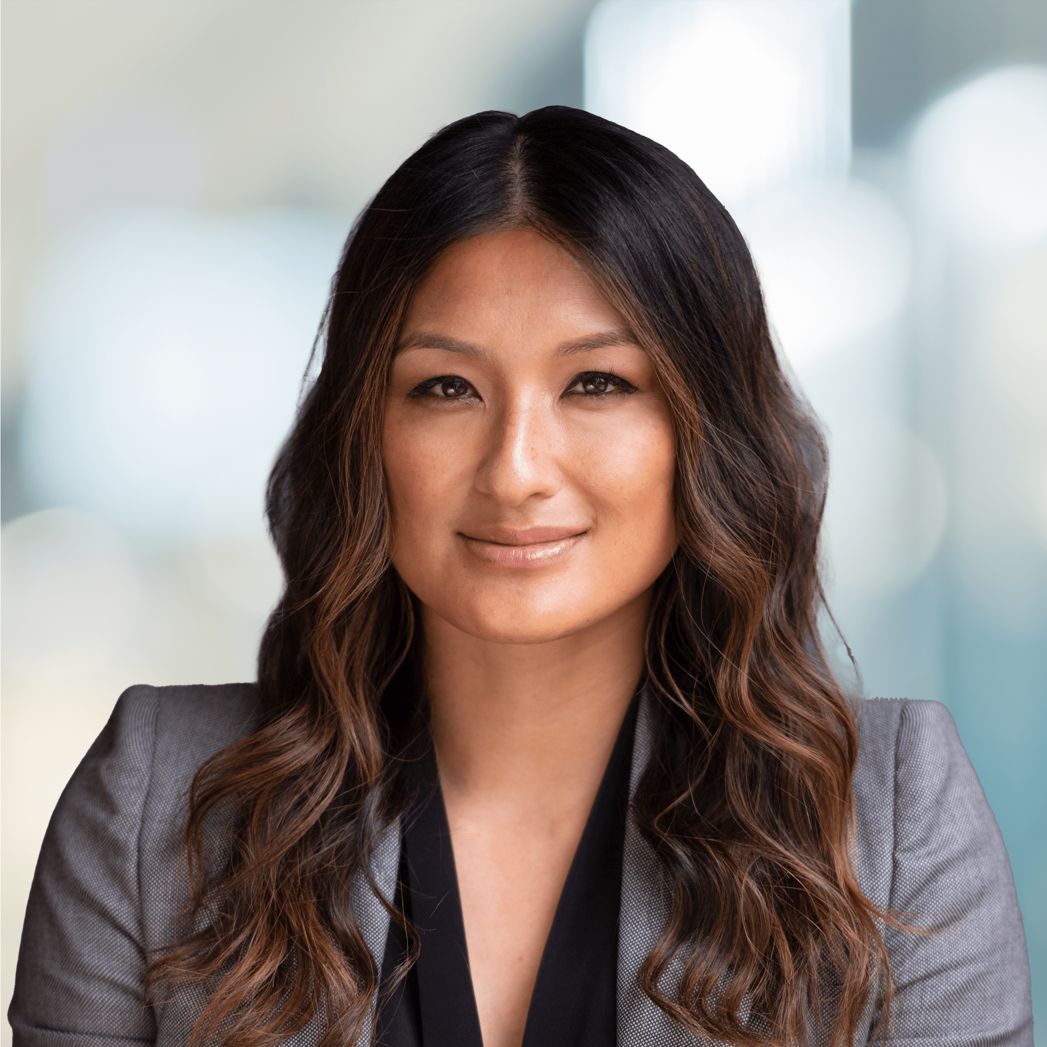 Headshot of Krystal Koo, Head of Sales and Marketing, smiling in front of a blurry background in a grey blazer