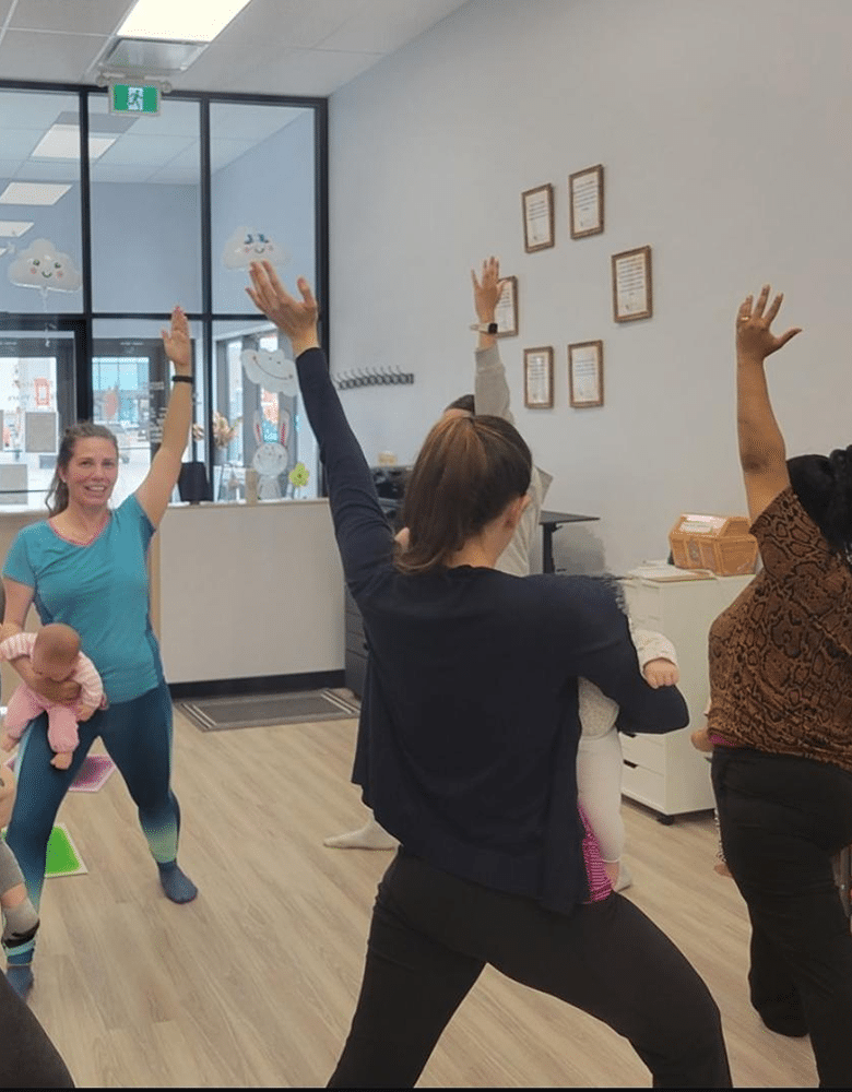 Four woman stand in a circle with their hands in the air for Mom and baby yoga, holding babies