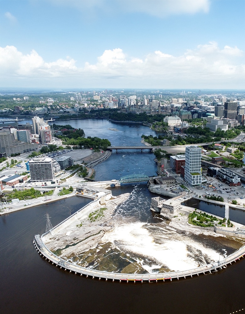 Zibi Project, a birds eye view of a city scape with tall buildings, and extension bridge with cars and lush greenery, with a sunrise in the background, featuring a river flowering beneath a charming bridge