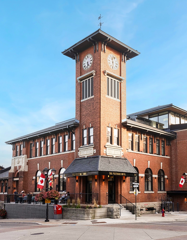 Exterior of the Postmark Hotel in Newmarket featuring a restored heritage brick façade with arched windows and elegant stone detailing; set along a charming Main Street backdrop with vintage lampposts and pedestrian-friendly walkways
