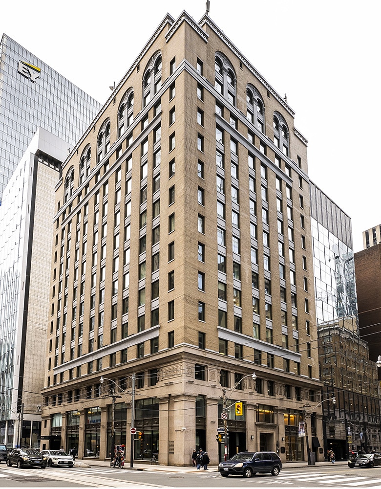 Exterior of 330 Bay Street in Toronto’s Financial District featuring a modernized glass façade with vertical fins and clean architectural lines; the mid-rise office building is framed by heritage masonry structures and urban streetscape elements.