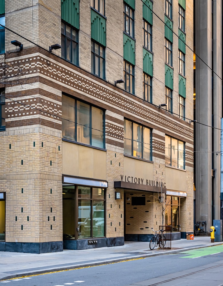 Exterior of the Victory Building at 80 Richmond Street West in Toronto showcasing its Art Deco architecture with detailed limestone façade, vertical lines emphasizing height, and heritage design elements; set within the Financial District, surrounded by urban streetscape and neighboring office towers